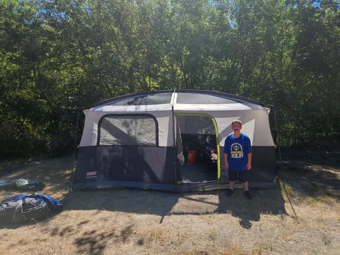 Wyatt standing beside a tent at a wooded campsite